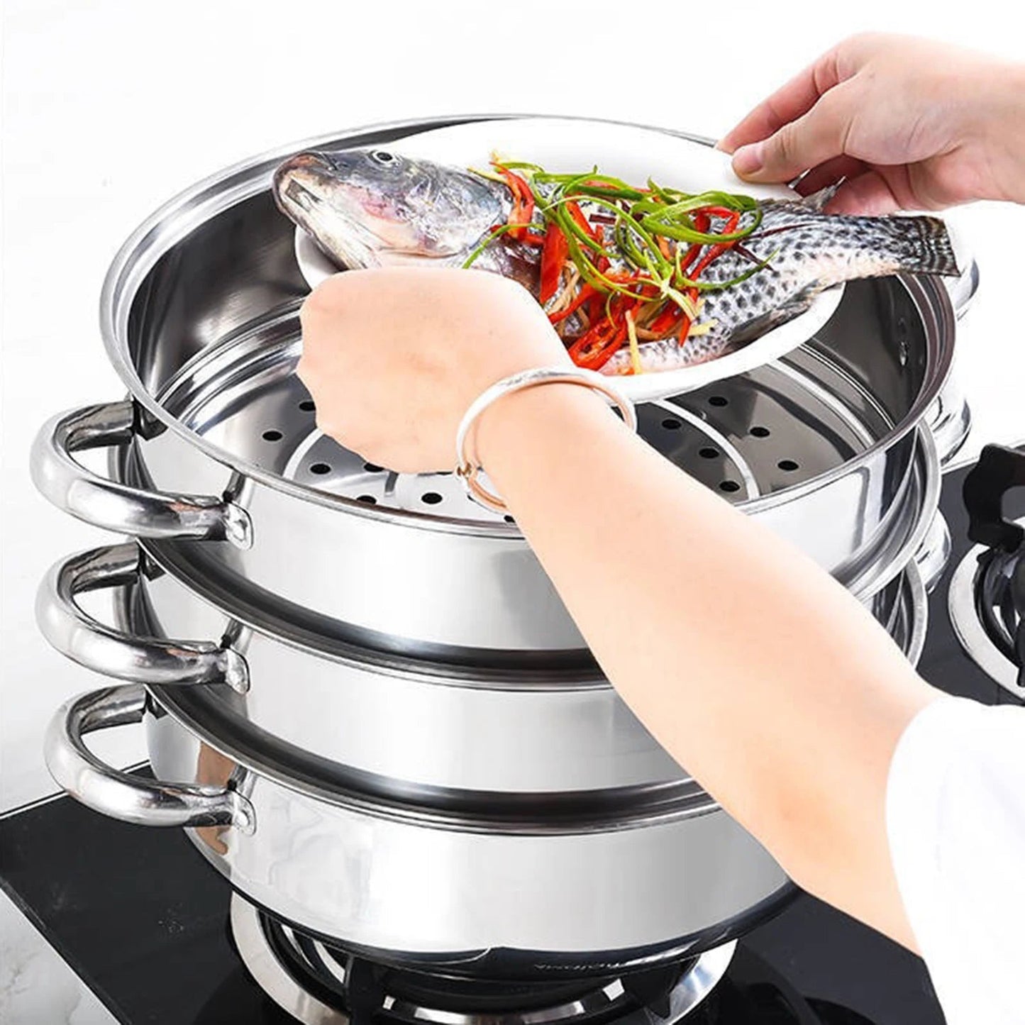 cuiseur- vapeur- 3 couches : une- main- mettant- poisson- dedans